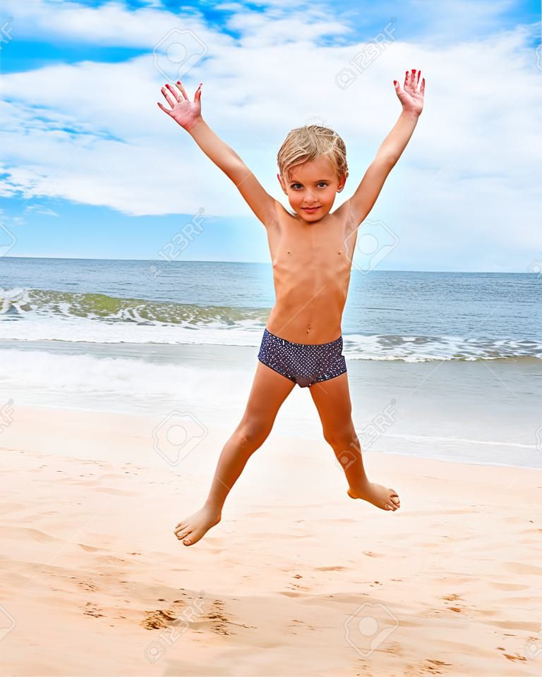 Springen Junge am Strand mit Blick aufs Meer im Hintergrund