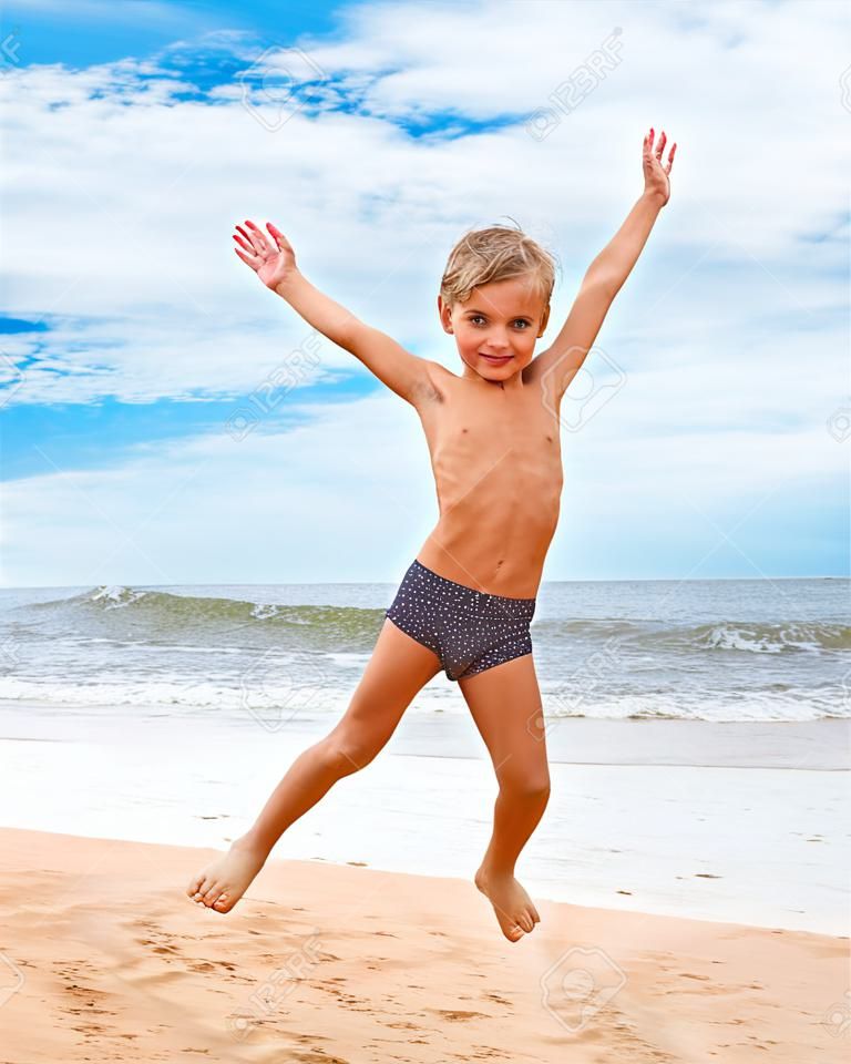 Мальчик прыгает на пляже с видом на море на фоне