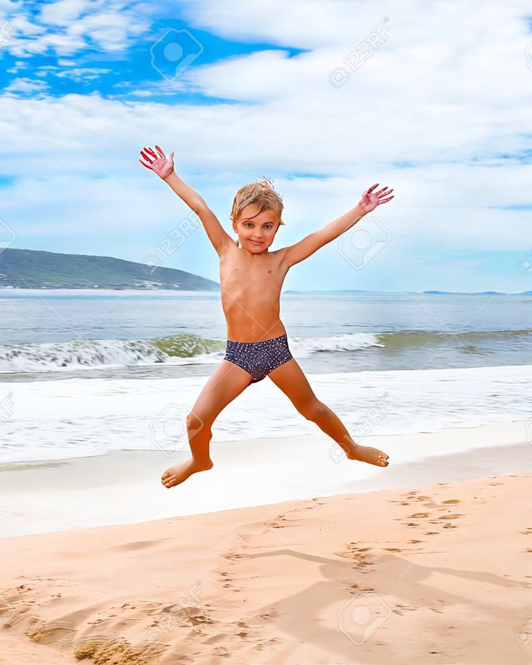 Springen Junge am Strand mit Blick aufs Meer im Hintergrund