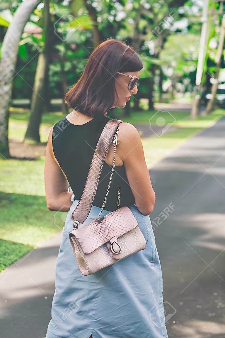 Fashionable woman with luxury snakeskin python handbag outside. Snakeskin fashion concept.