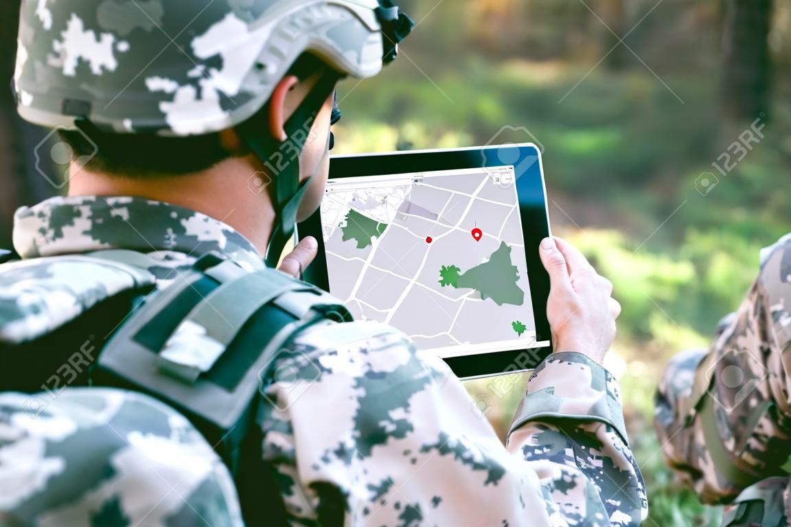 Солдат с помощью карты на планшете для ориентации в лесу