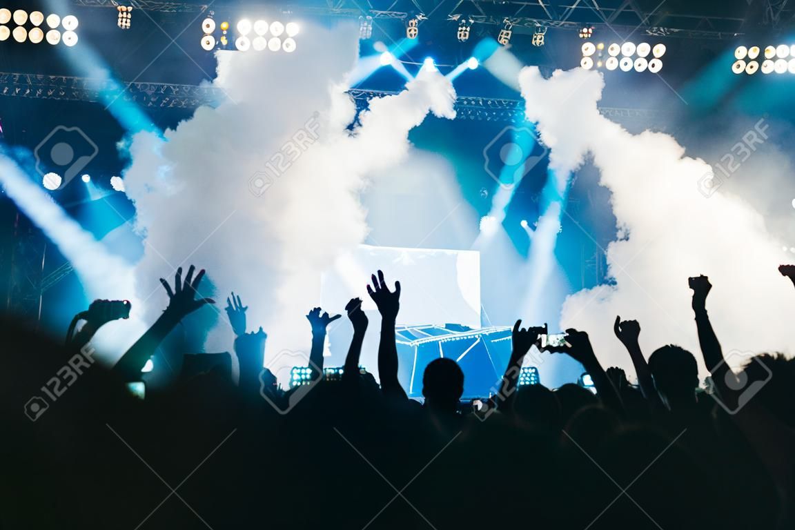 Luci del palcoscenico e folla di pubblico con le mani alzate a un festival musicale. I fan si godono le vibrazioni della festa.