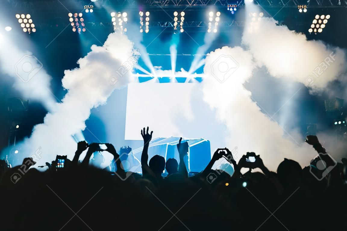 Luci del palcoscenico e folla di pubblico con le mani alzate a un festival musicale. I fan si godono le vibrazioni della festa.