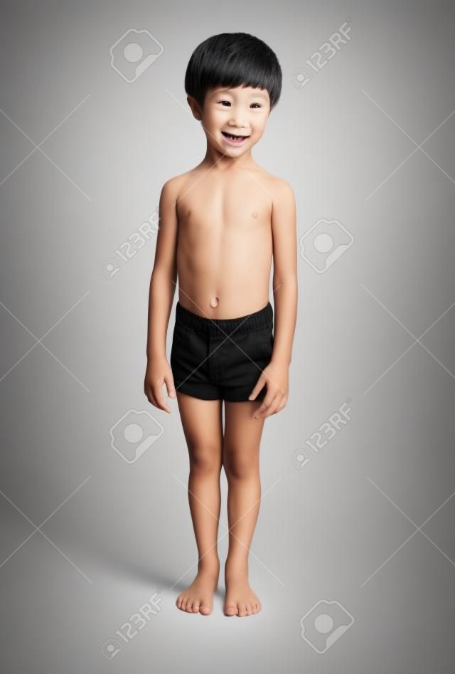 Netter kleiner asiatischer 3-jähriger Kleinkindjunge, der schwarze Hosen trägt, die auf weißem Hintergrund stehen.