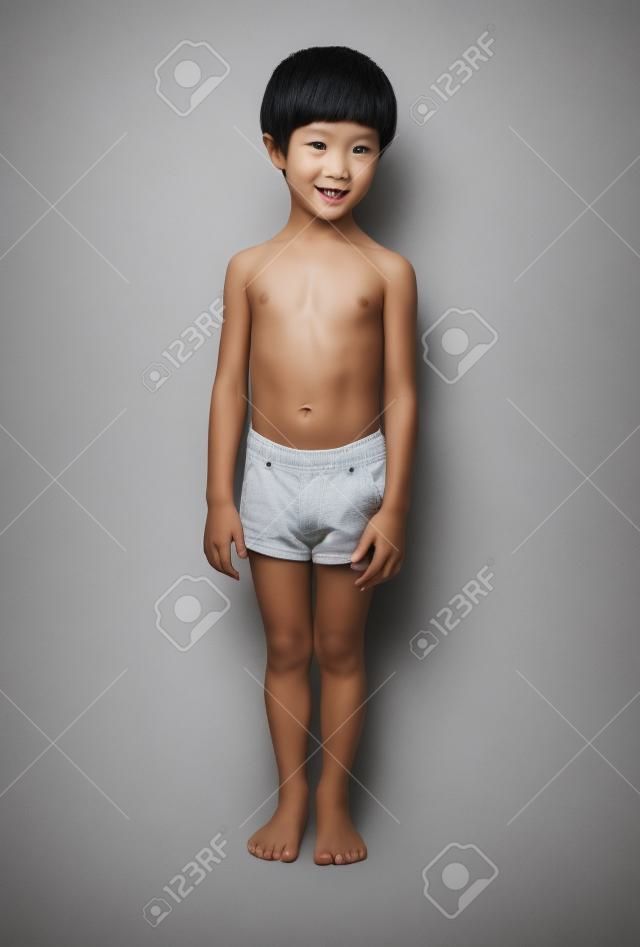 Netter kleiner asiatischer 3-jähriger Kleinkindjunge, der schwarze Hosen trägt, die auf weißem Hintergrund stehen.