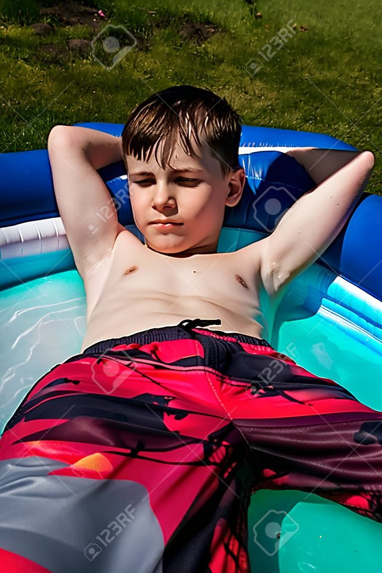 Shirtless preteen caucasian boy laying in a paddling pool