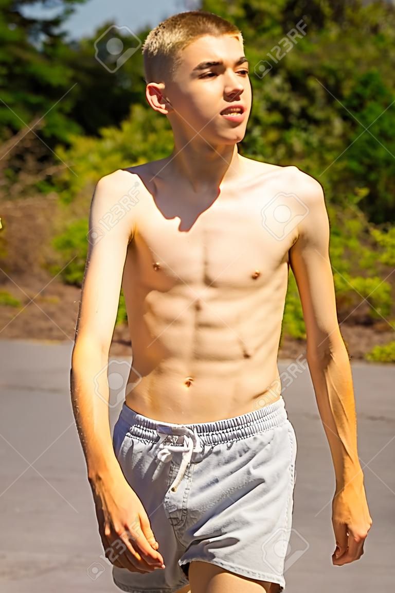An eighteen year old teenage boy walking outside on a warm summer's day while shirtless