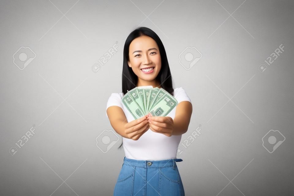 Feliz y sonriente dueña de una empresa asiática, gerente de la tienda mostrando el dinero que ganó en la tienda en línea, sosteniendo efectivo y regocijándose, mostrando sus ingresos, de fondo blanco