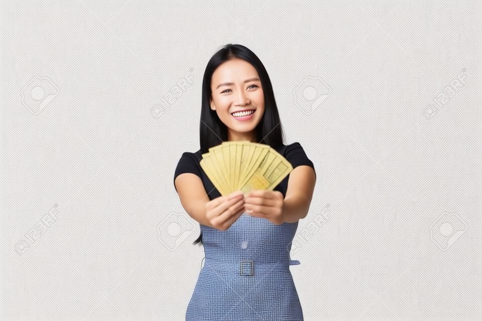 Felice sorridente imprenditore femminile asiatico, responsabile del negozio che mostra i soldi che ha guadagnato nel negozio online, tenendo contanti e gioendo, sfoggiare con il suo reddito, in piedi su sfondo bianco