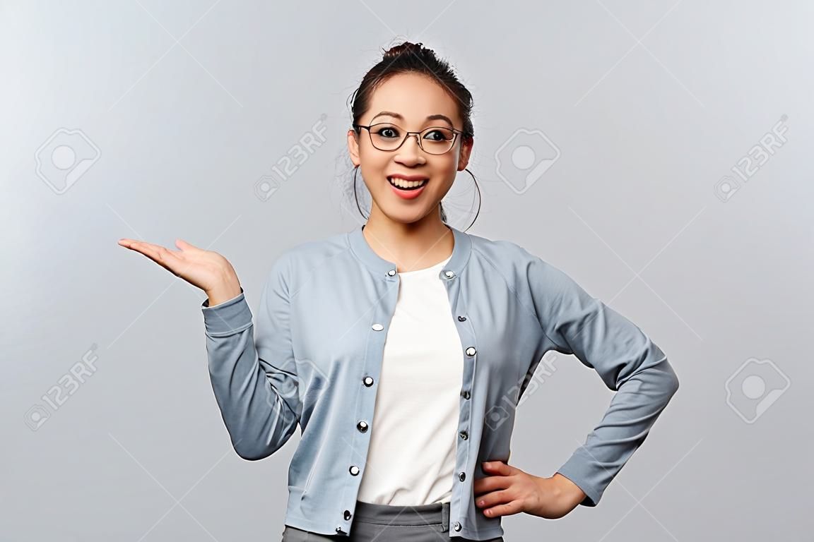 Koncepcja stylu życia, ludzi i emocji. wesoła, szczęśliwa azjatka w okularach przedstawia nowy produkt firmy lub baner, wskazując, trzymając promocję pod ręką nad lewą stroną miejsca na kopię