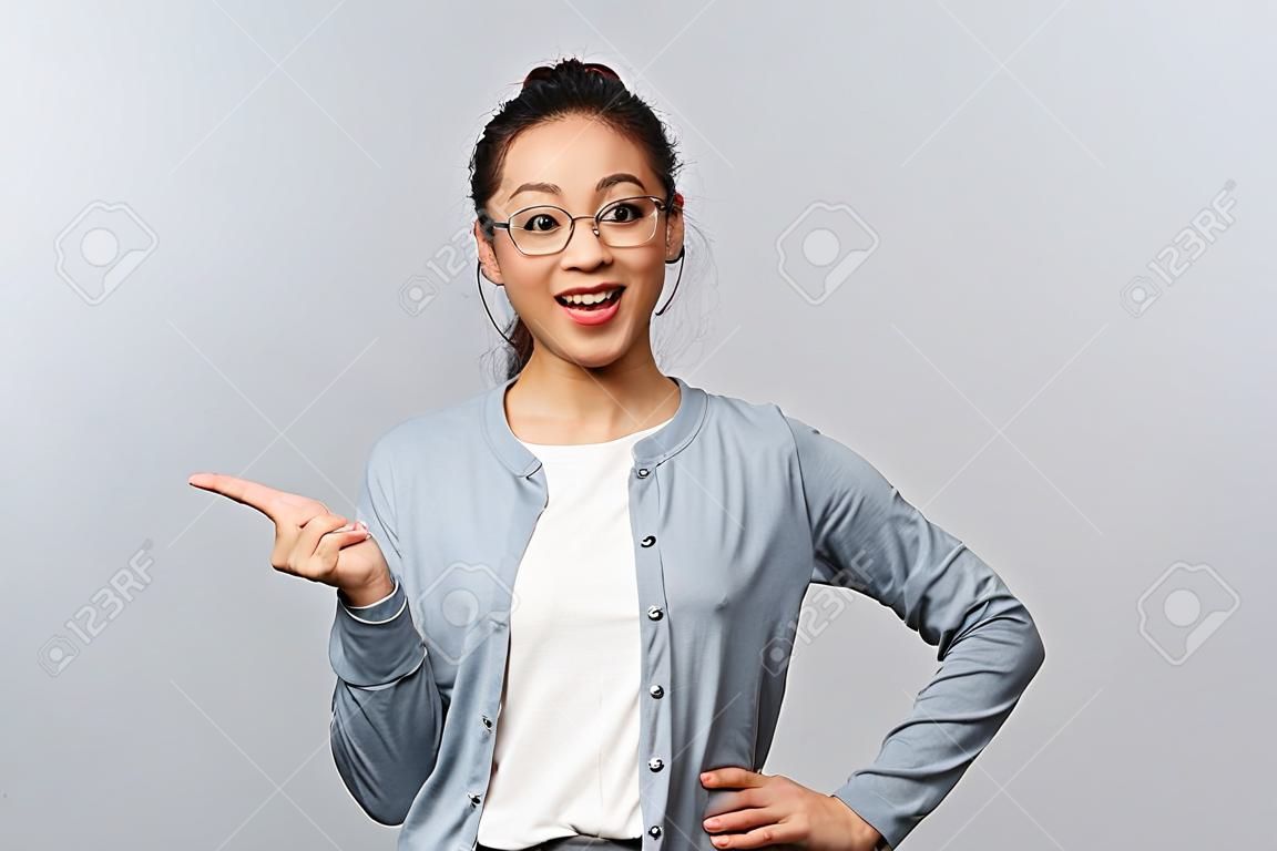 Koncepcja stylu życia, ludzi i emocji. wesoła, szczęśliwa azjatka w okularach przedstawia nowy produkt firmy lub baner, wskazując, trzymając promocję pod ręką nad lewą stroną miejsca na kopię