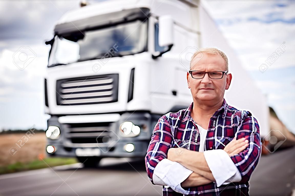Portret kierowcy ciężarówki ze skrzyżowanymi ramionami stojących z przodu ciężarówki.