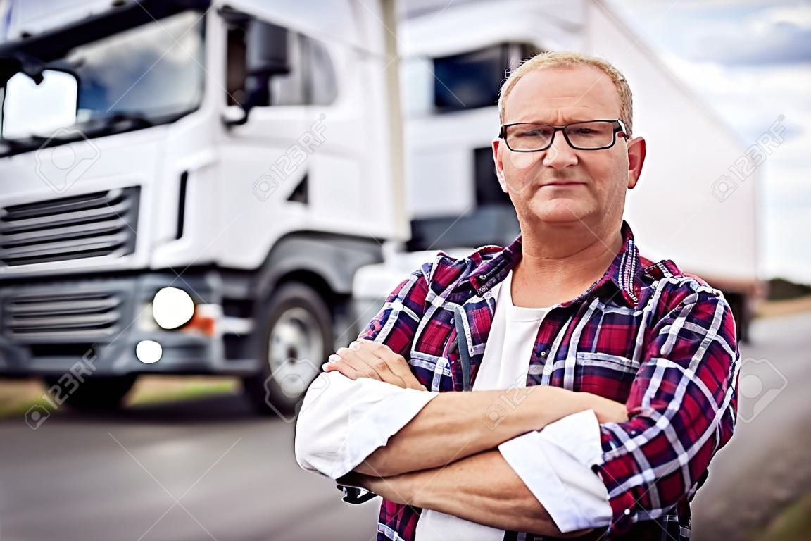 Portret kierowcy ciężarówki ze skrzyżowanymi ramionami stojących z przodu ciężarówki.