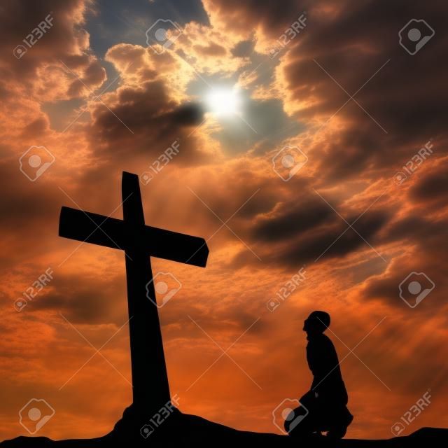 Concept conceptual black cross or religion symbol man silhouette in rocks over a sunset sky with sunlight clouds background