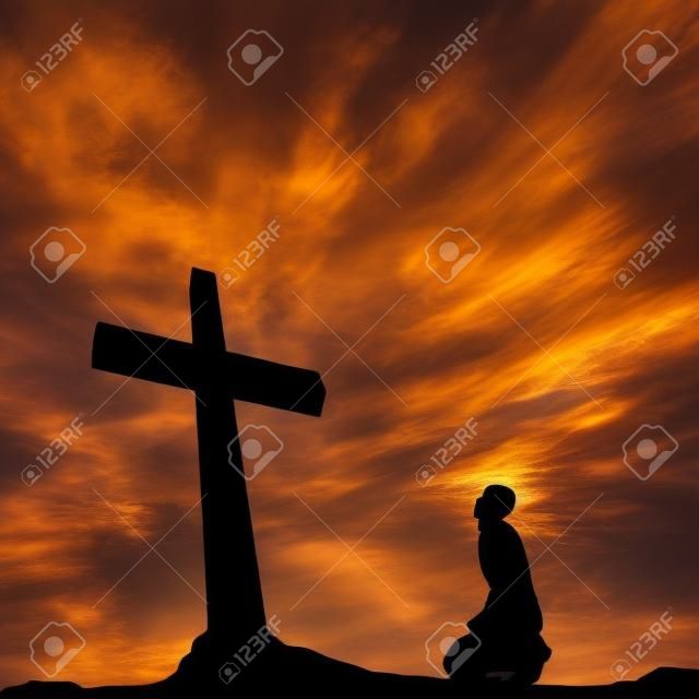 Concept conceptual black cross or religion symbol man silhouette in rocks over a sunset sky with sunlight clouds background
