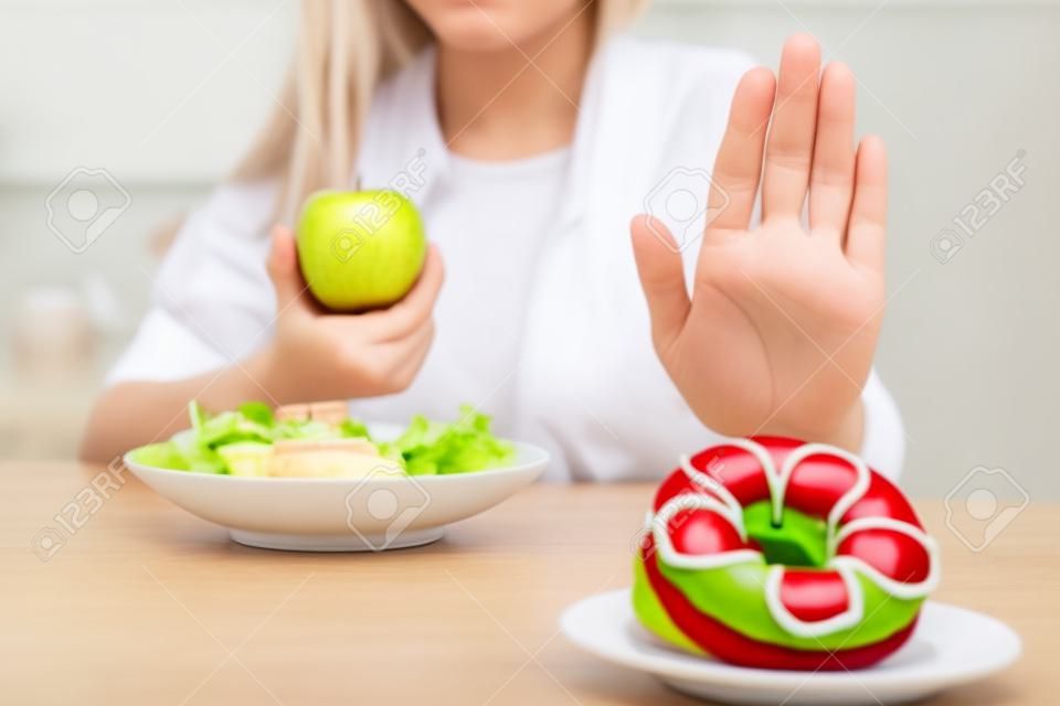 Diät-Konzept. Gesunde Frauen lehnen ungesunde Lebensmittel wie Donuts oder Desserts mit den Händen ab. Schlanke Frauen entscheiden sich für gesunde Lebensmittel und hohe Vitamine wie Äpfel und Gemüsesalate.
