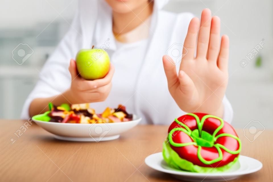 Diät-Konzept. Gesunde Frauen lehnen ungesunde Lebensmittel wie Donuts oder Desserts mit den Händen ab. Schlanke Frauen entscheiden sich für gesunde Lebensmittel und hohe Vitamine wie Äpfel und Gemüsesalate.
