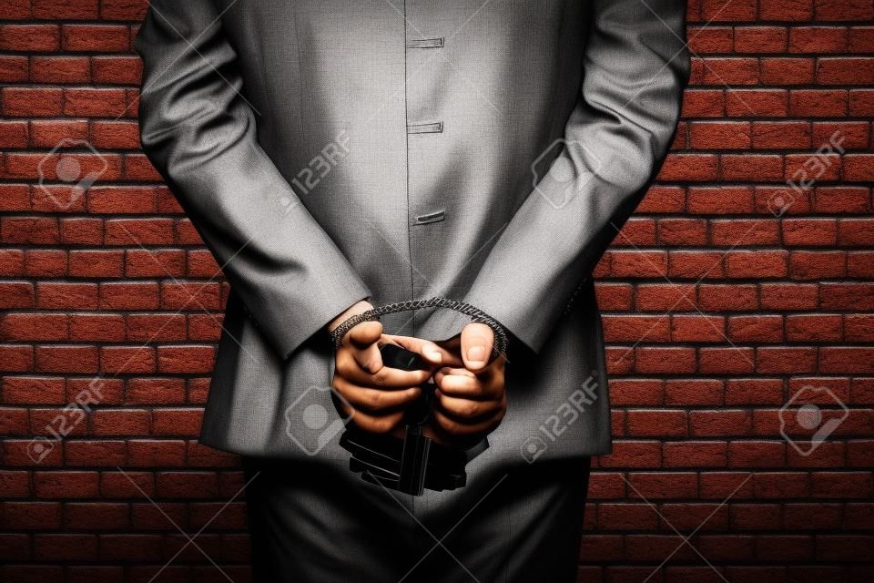刑務所で手錠でお金の請求書を保持しているブラジル人男性。腐敗、腐敗した政治家、違法な事業の概念。レンガの背景。