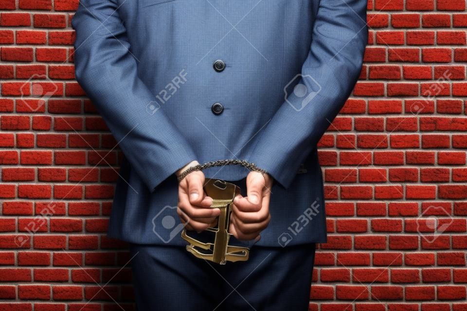 Brazilian man holding bills of money with a handcuff in a jail. concept of corruption, corrupt politicians, illegal businesses. brick background.