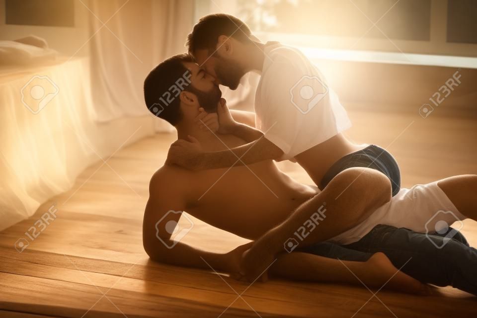 Leidenschaftliche Paar küsst, Jungen und Mädchen sitzen auf Holzboden in der Nähe des zerwühlten Bett gegenüber dem Fenster.