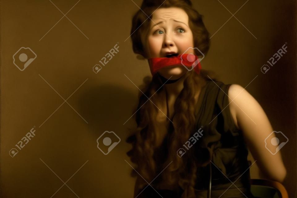 Erschrockene junge Frau an einen Stuhl gefesselt und mit einem Knebel in den Mund