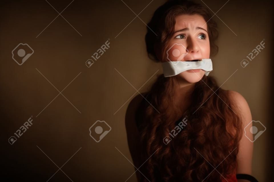mujer joven aterrorizada en una habitación vacía, después de su boca amordazada