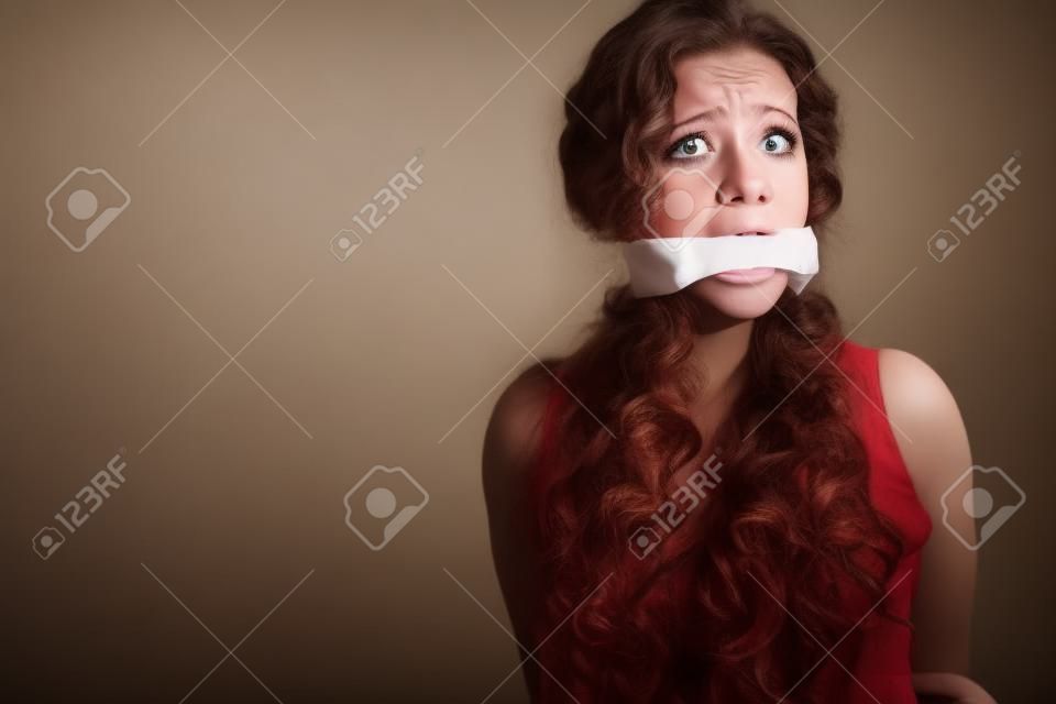 mujer joven aterrorizada en una habitación vacía, después de su boca amordazada