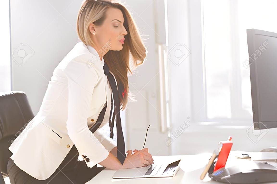 Lövés egy gyönyörű nő ül egy asztal egy irodában, és kezében elegáns férfi nyakkendő