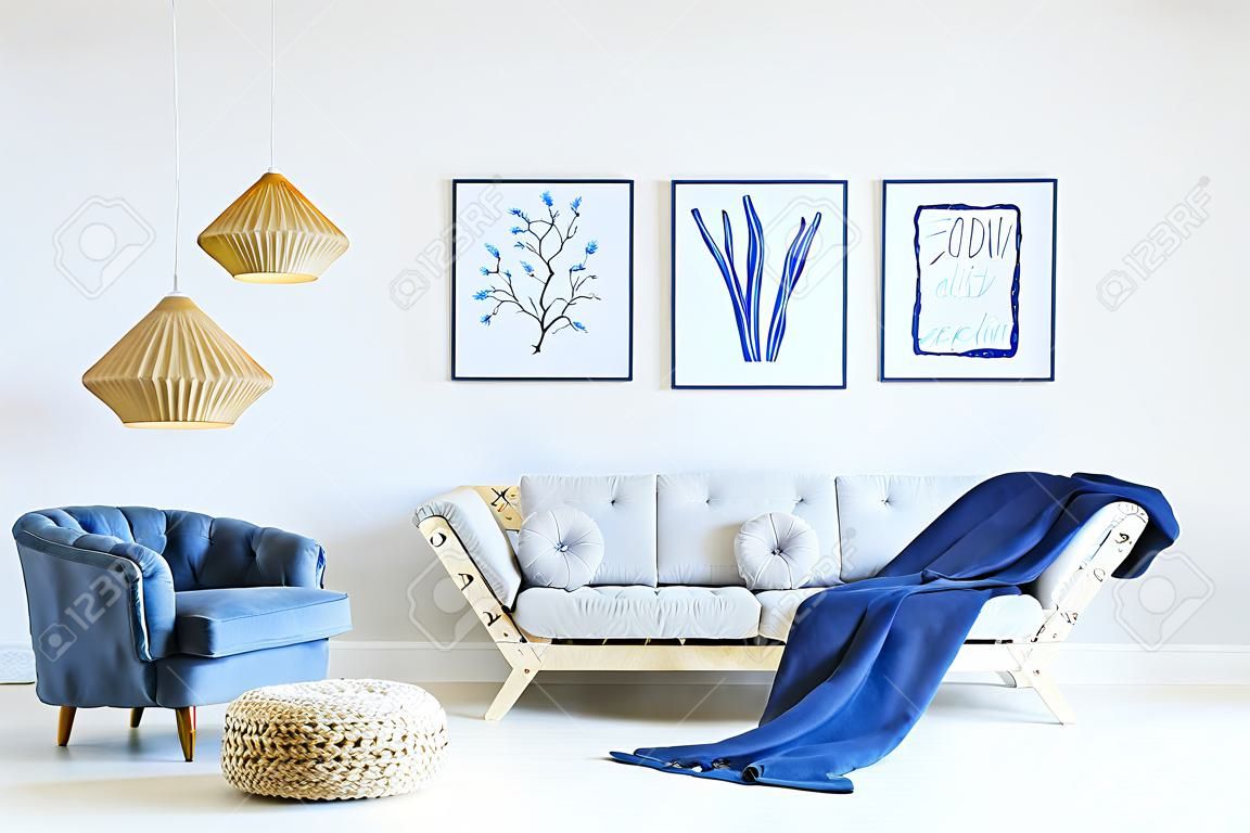 Biały i niebieski pokój dzienny z sofą, fotelem, lampą, plakatami