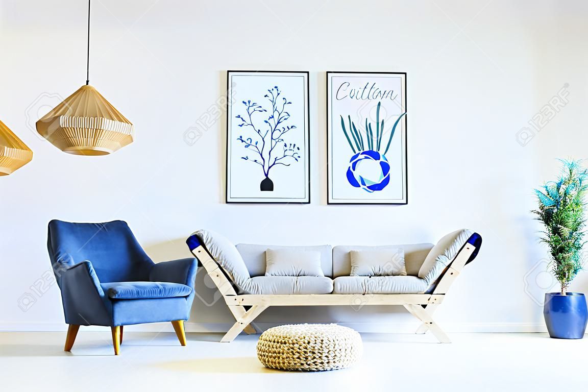 Sala de estar branca e azul com sofá, poltrona, lâmpada, cartazes