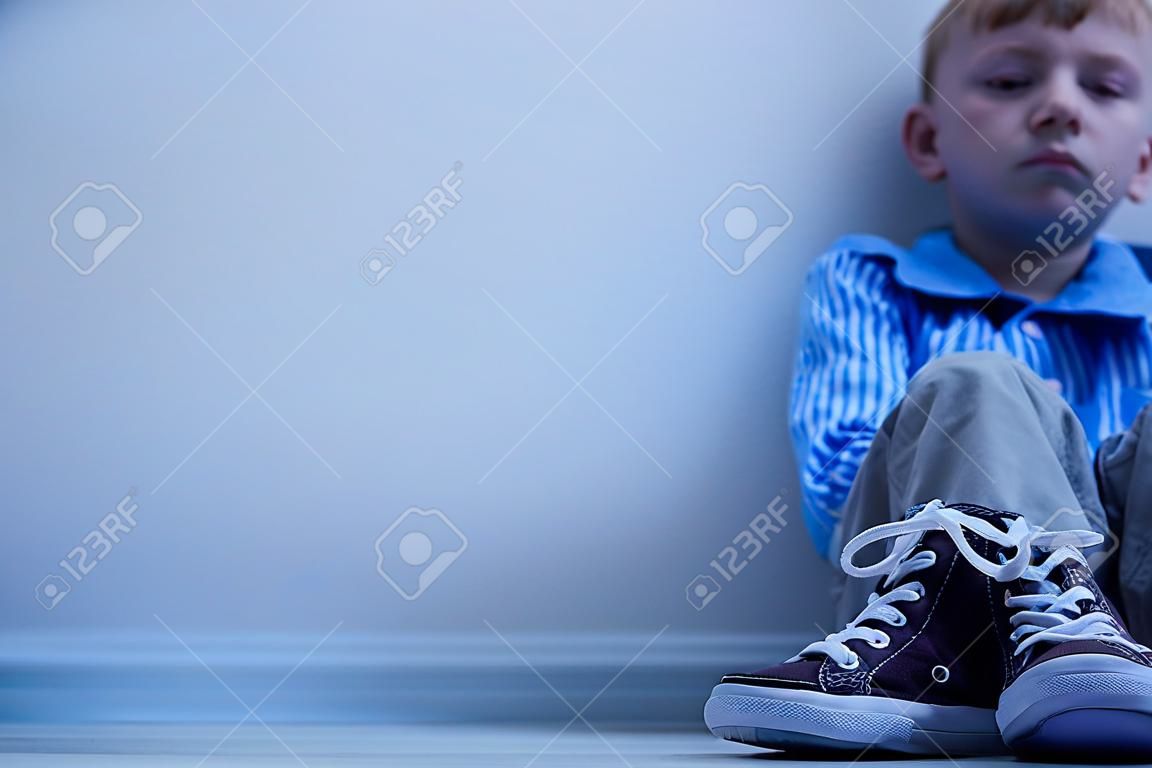 Smutny chłopiec w trampkach z zespołem aspergera siedzi sam w swoim pokoju