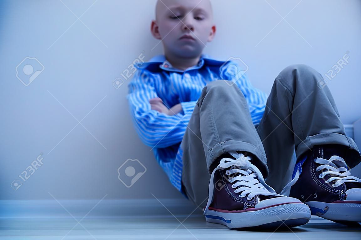 Sad boy in sneakers with asperger's syndrome sits alone in his room