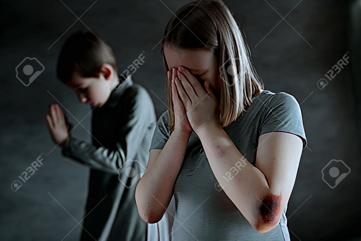 Young girl with bruises and boy crying alone in the dark room