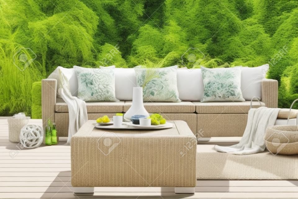 Rattan table and pillows on couch standing on a patio in the garden during summer. Real photo