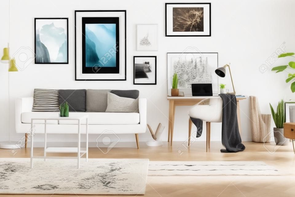 Framed photos gallery on a white wall of a hipster living room interior and workspace with laptop on a wooden desk