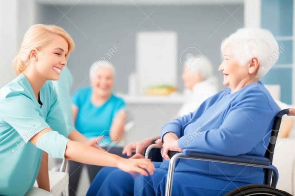 Young nurse supporting an elderly woman on wheelchair. Nursing home concept
