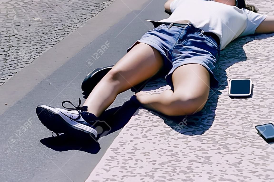 Ragazza incosciente sdraiata su una strada accanto al suo cellulare