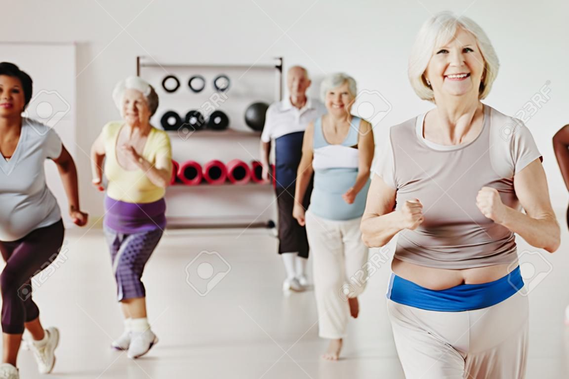 Femme âgée souriante faisant de l'exercice avec un groupe de personnes âgées actives dans un centre de remise en forme
