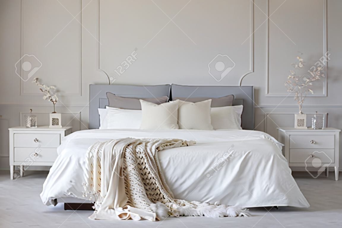 花瓶の2つの木製のベッドサイドテーブルの花の間に白いシーツと毛布を持つキングサイズベッド