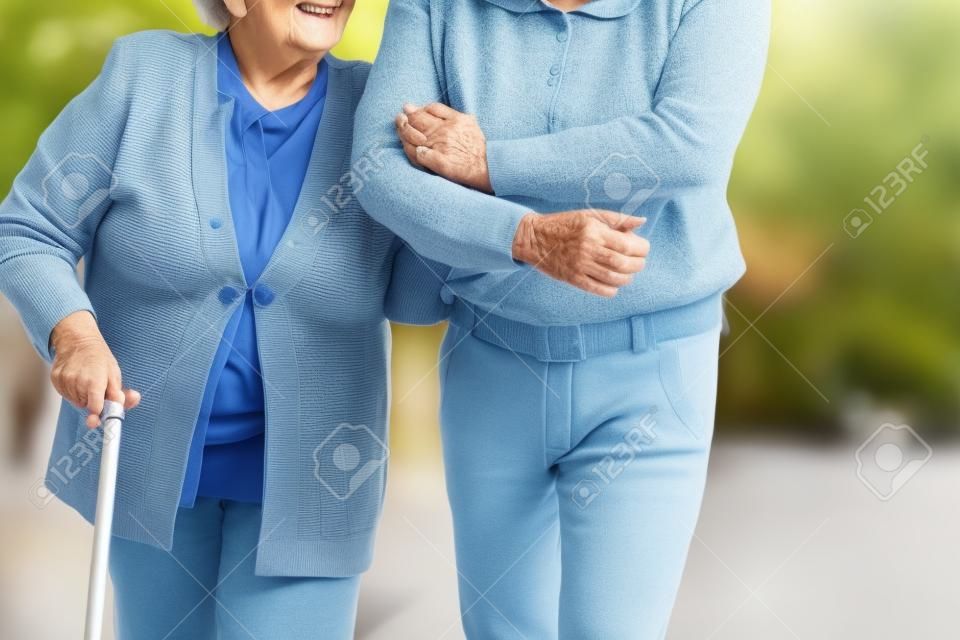 Close-up on person supporting smiling senior woman with walking stick
