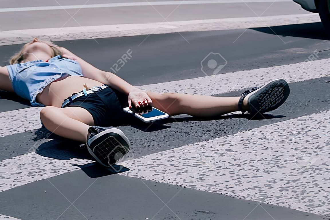 Teenage girl with mobile phone lying on the street after terrible car crash on pedestrian crossing