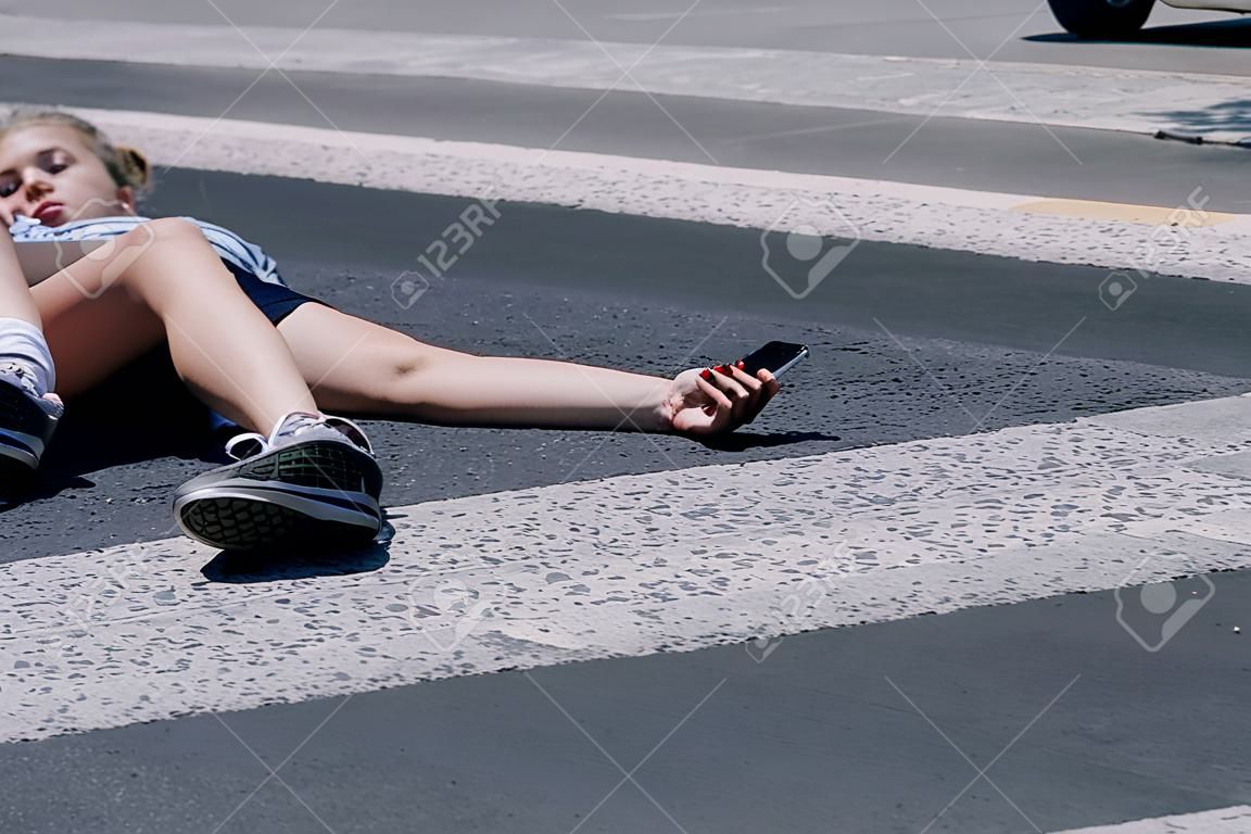 Adolescente con teléfono móvil tirado en la calle después de un terrible accidente automovilístico en el paso de peatones