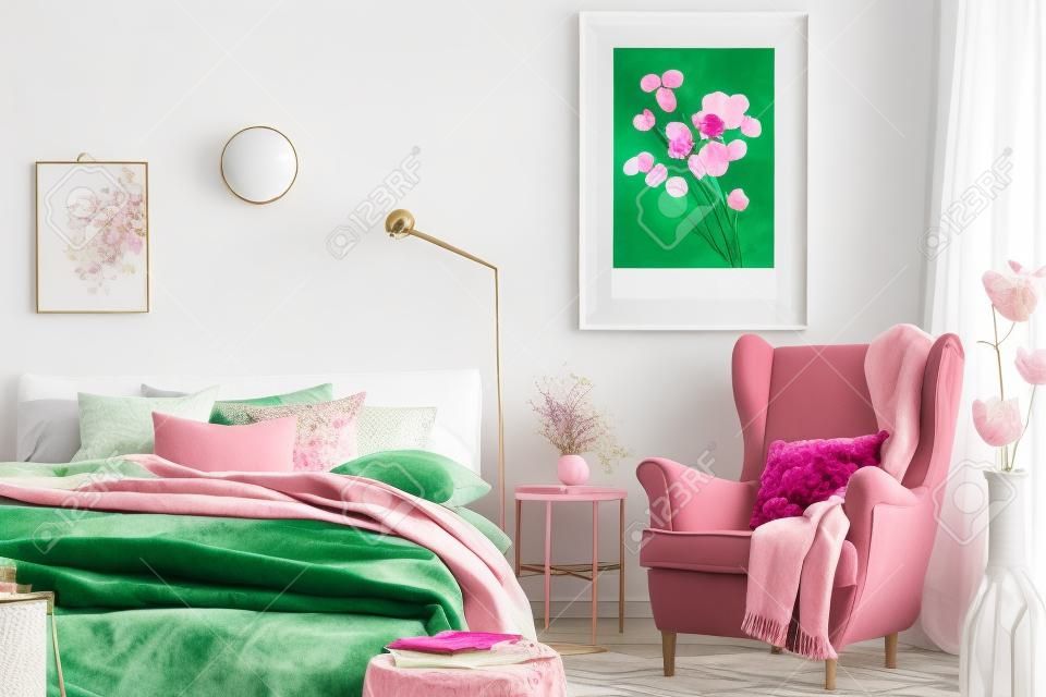Floral pillow and pink blanket on emerald green comfortable armchair in fashionable bedroom