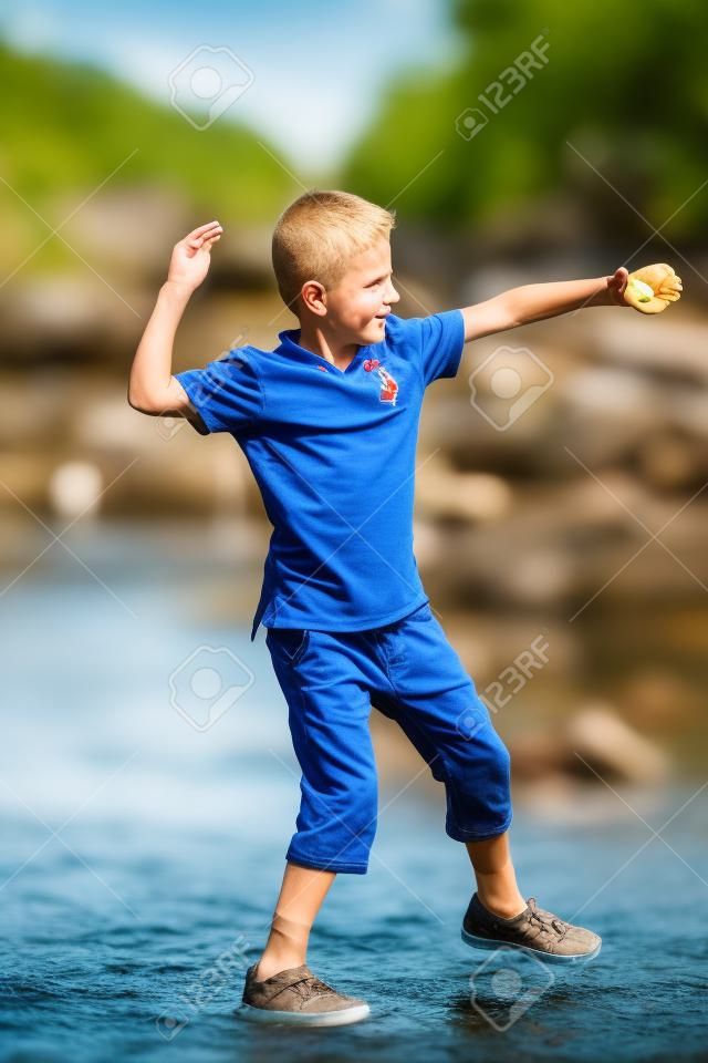 挪威阳光明媚的夏日，男孩在河里扔石头。