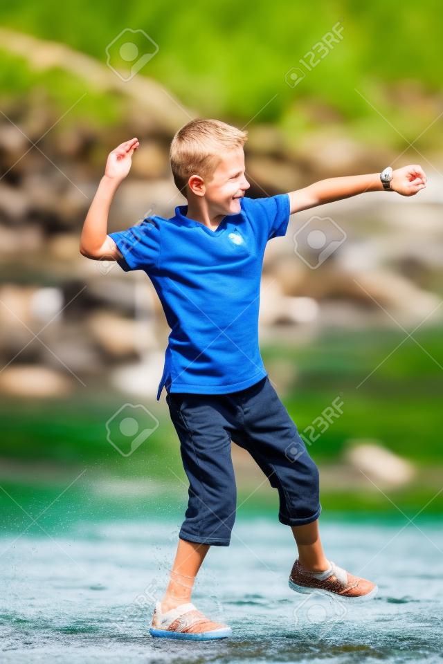 Boy throwing stone in the river on a sunny summer day in Norway.