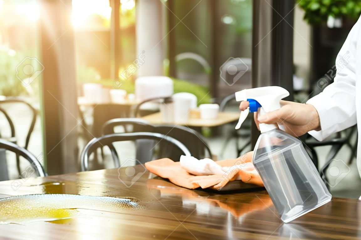 Kelner czyści stół środkiem dezynfekującym w restauracji