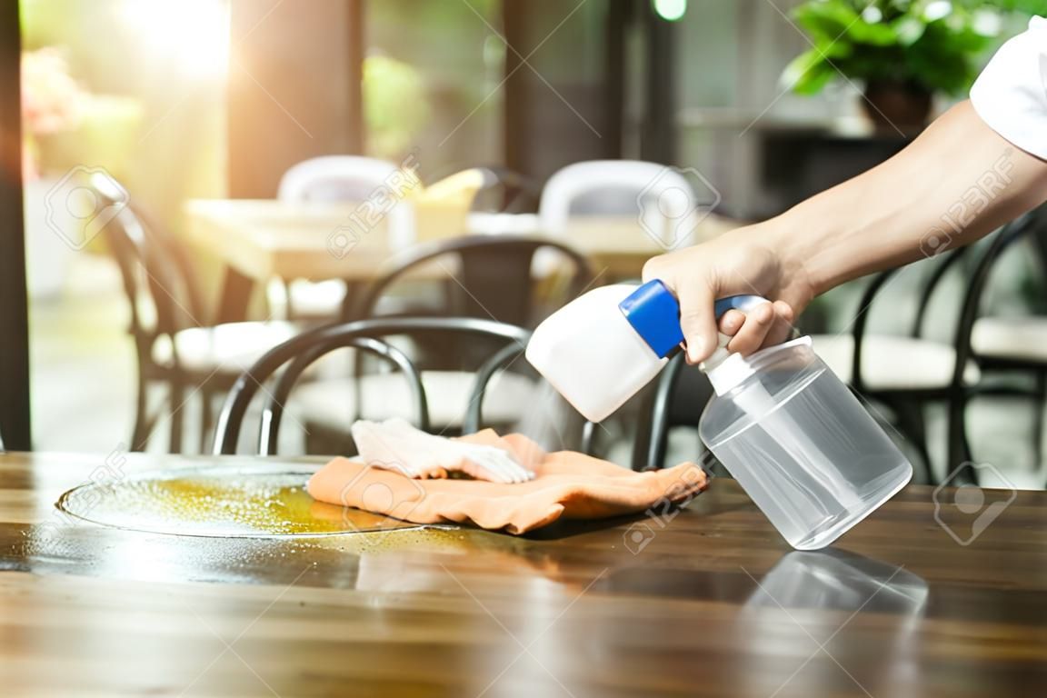 Cameriere che pulisce il tavolo con spray disinfettante in un ristorante