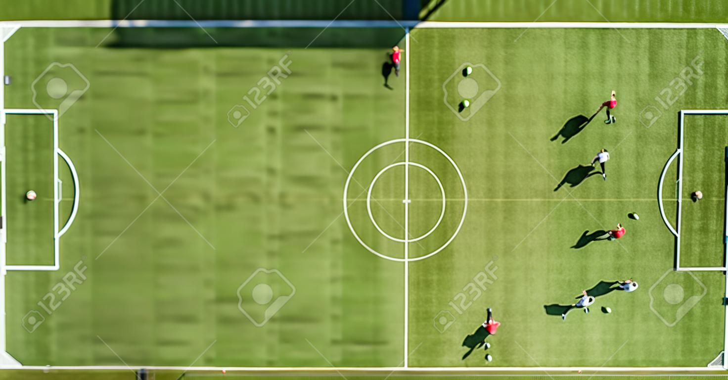 Top down aerial view of green football sports field and players playing football. Drone taken image of small unrecognizable sportsmen on grass covered stadium during sport activities.