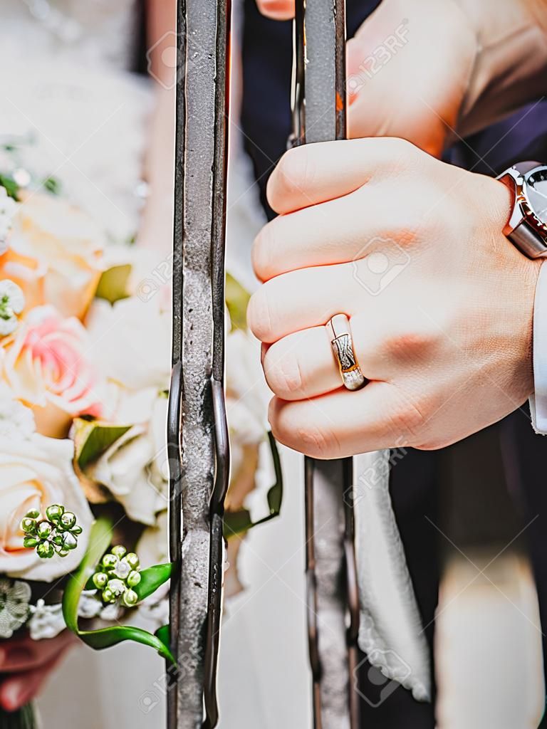 Een pas getrouwd stel legt zijn handen op een ijzeren staaf met hun trouwringen.