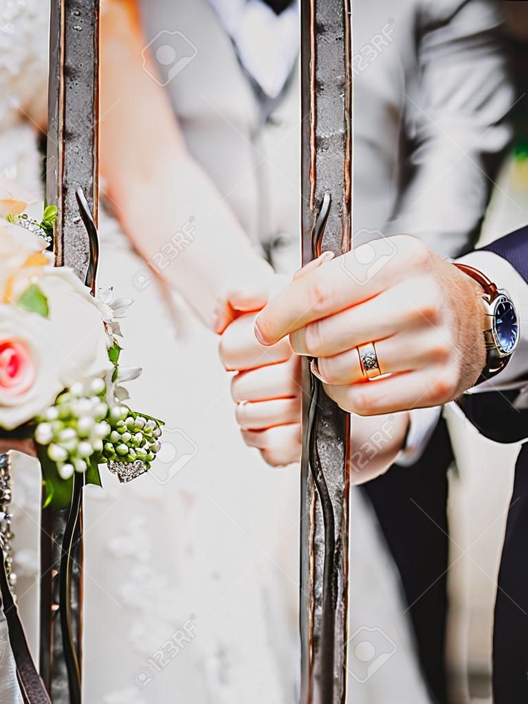 A newly-married couple puts their hands on an iron bar showing their wedding rings.
